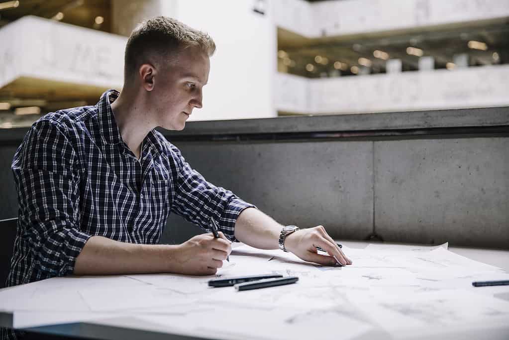 Male architect sketching architectural details with pencil on tracing paper
