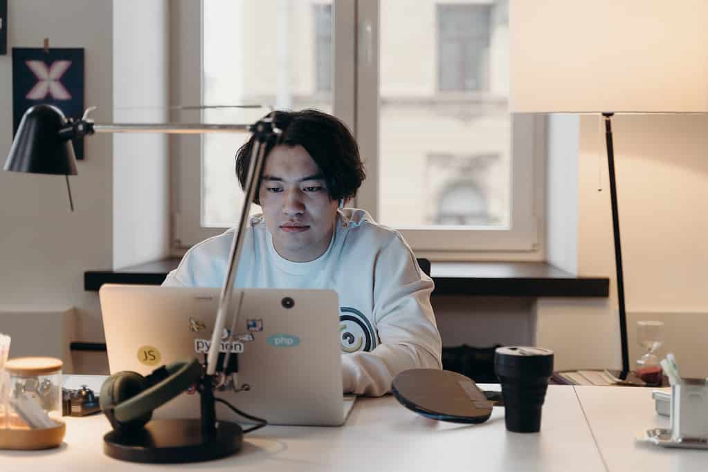 Young creative professional working on laptop in minimalist studio workspace with desk lamp