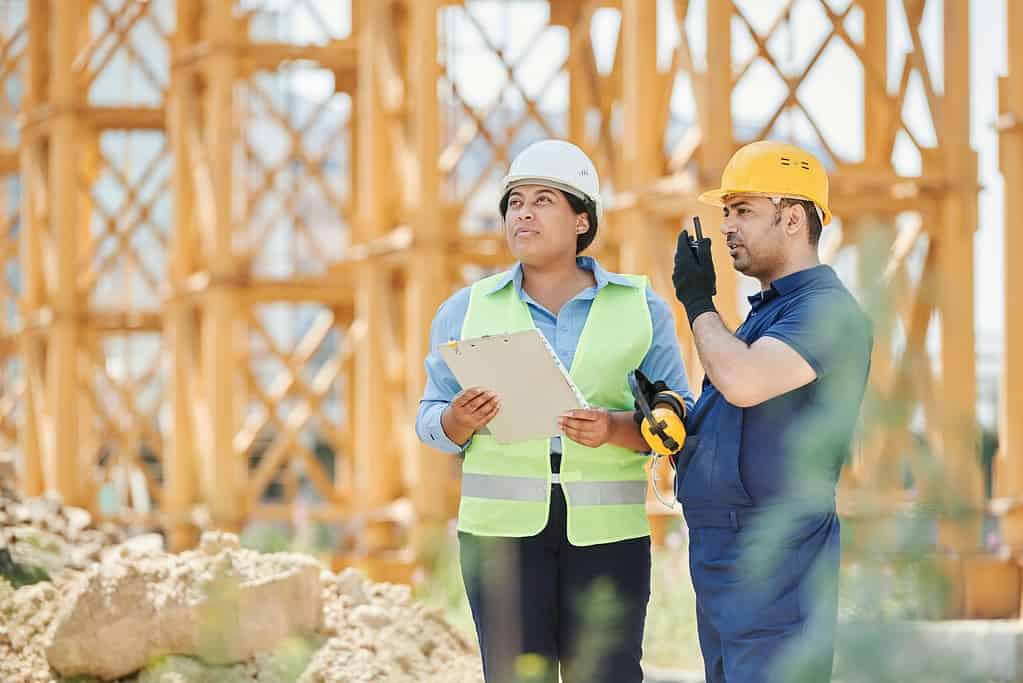 Construction workers in hard hats and hi-vis vests reviewing architectural plans on building site