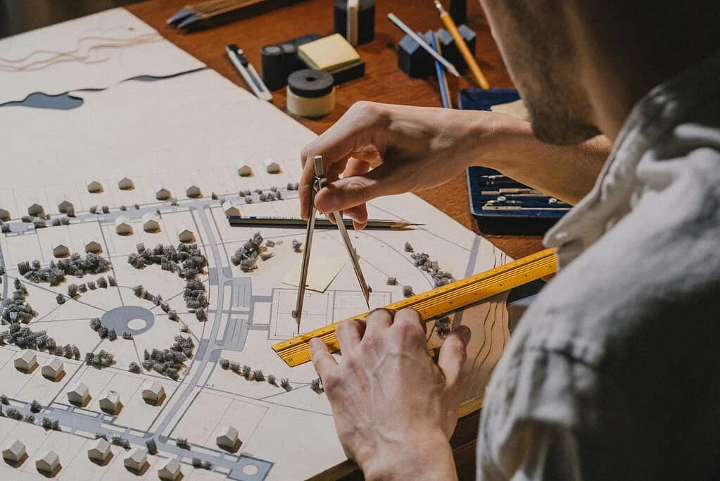 Architectural site plans and blueprints spread across desk with drafting tools and scale ruler