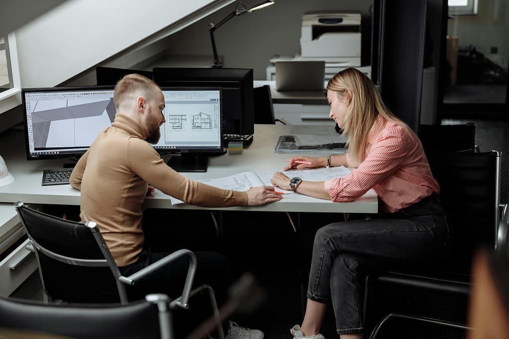 Two architects collaborating at workstation reviewing project designs on computer screen
