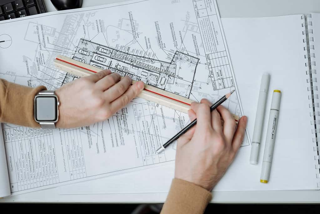 Close-up of architect's hands marking up technical drawings with pen alongside phone and drafting tools