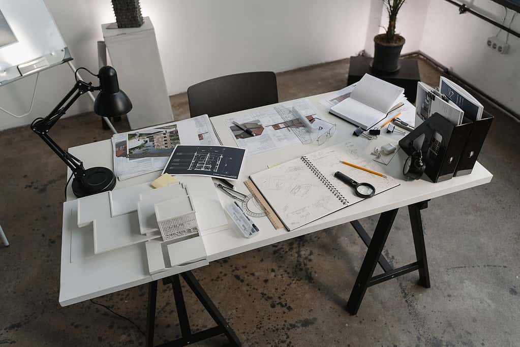 Overhead view of architect's workspace with blueprints, laptop and drafting equipment spread across desk