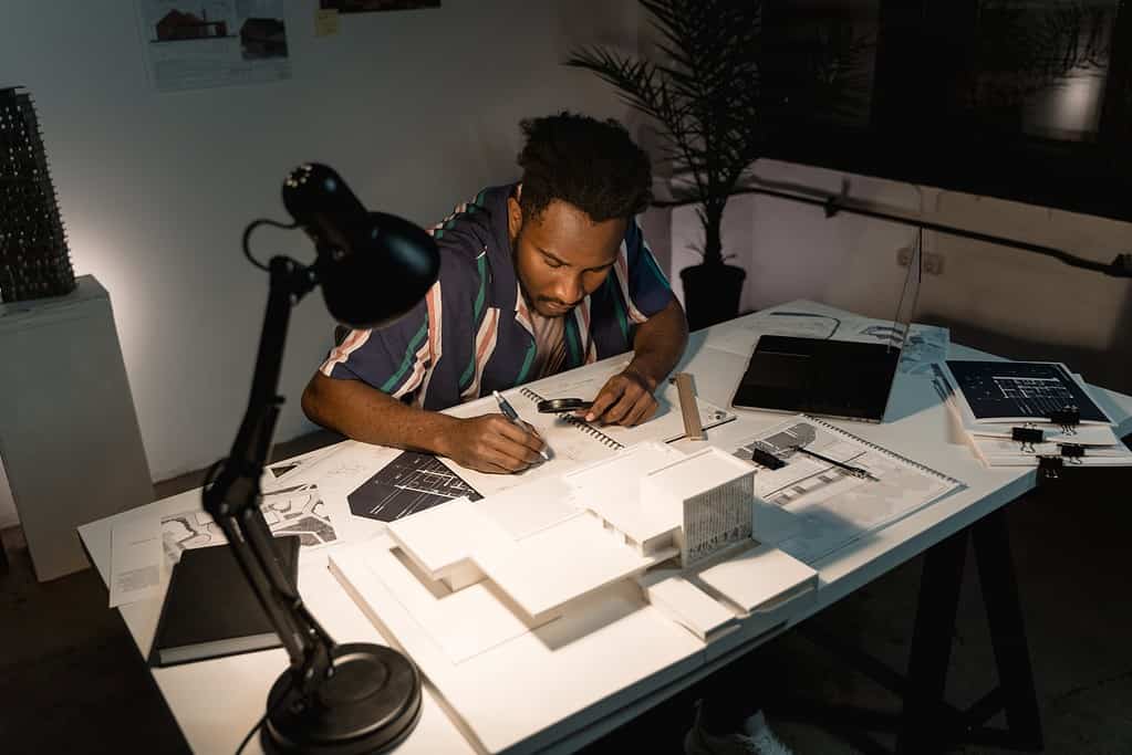 Architect working late into evening reviewing technical drawings under desk lamp illumination