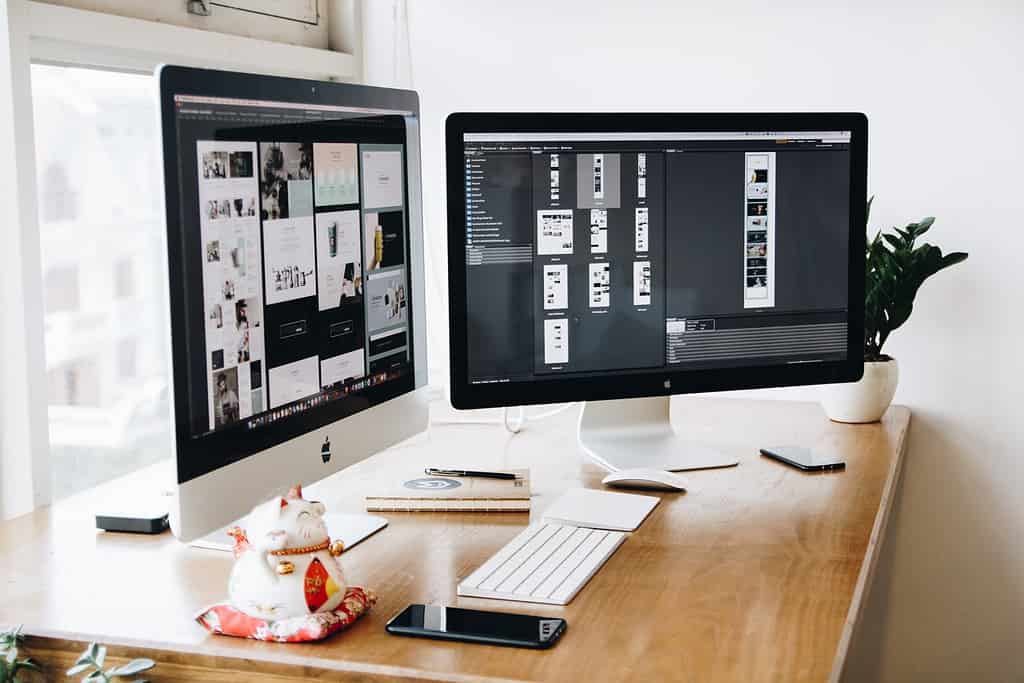 Designer's desktop setup with large monitor displaying creative software and portfolio layouts